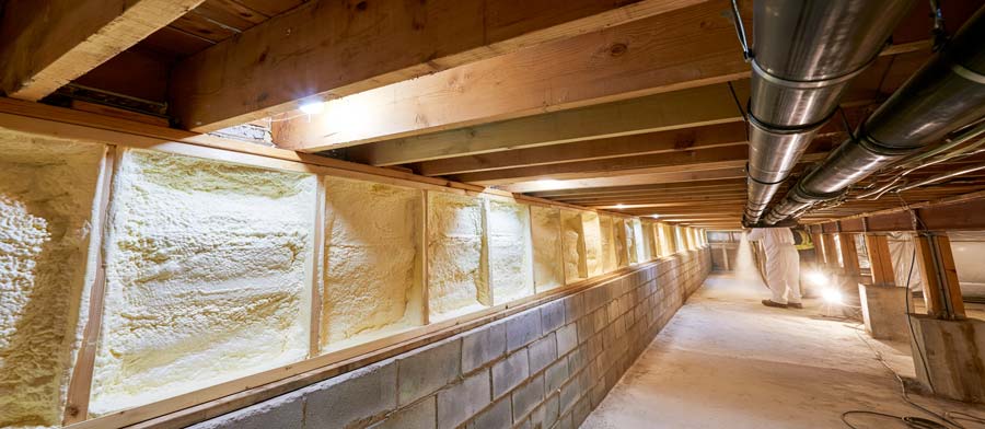 floor joist bays above a block foundation wall, several bays freshly sealed with pale yellow closed-cell spray foam
