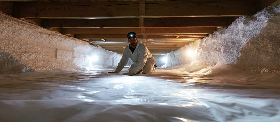 professional contractor in protective suit and headlamp working inside a residential crawl space