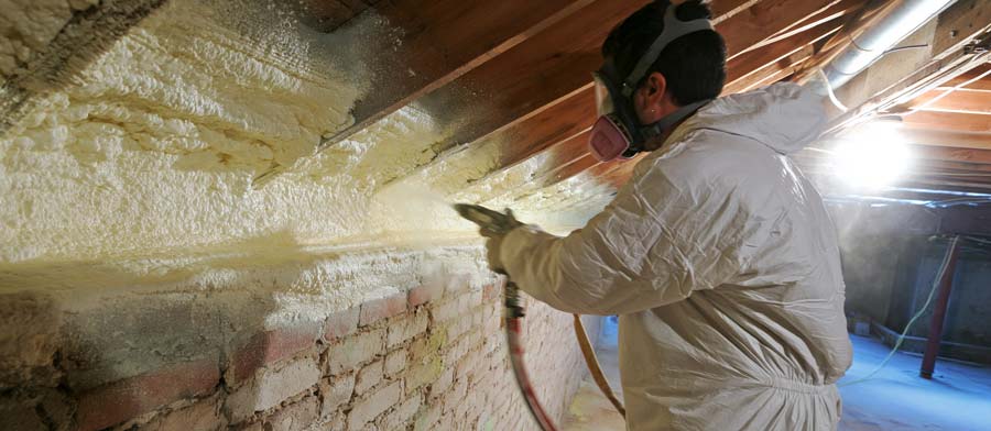 professional insulation contractor in white protective suit and full-face respirator spraying closed-cell polyurethane foam