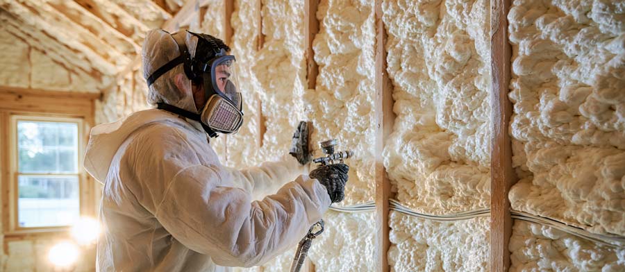 professional insulation contractor in protective suit and respirator spraying open-cell polyurethane foam into open stud wall cavities